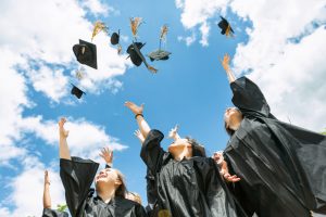 Students in graduation robes throwing hats into a blue sky with white clouds