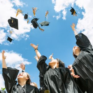 Students in graduation robes throwing hats into a blue sky with white clouds