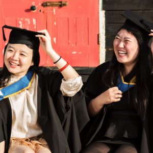Two female students smile wearing their graduation robes and hats