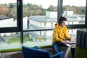 A student wearing a yellow hoody working on a laptop