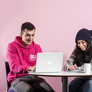 Two students sitting at a table looking at a laptop