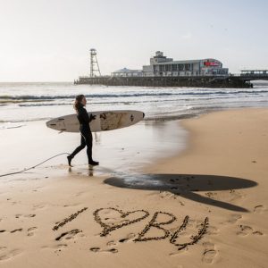 Surfer on Bournemouth beach with I heart BU written in the sand