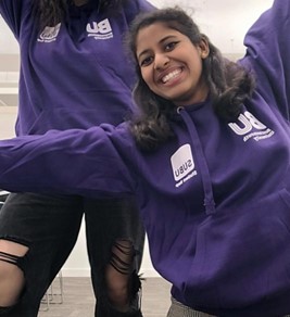 Madhurya stands next to another person wearing a purple BU hoodie and smiling with her arms out wide