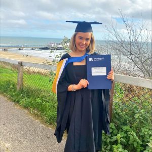 Lauren Jones in her graduation gown with Bournemouth Pier behind her