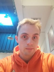 Student Tom poses for a selfie in a bright orange hoodie.