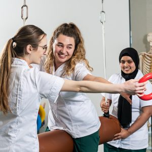 3 female occupational therapy students are conducting a balance exercise with one sat holding a hoop in their hand.