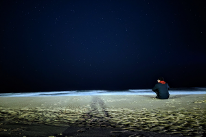 Student Muhammad sitting on the beach facing the sea at night with a starry sky 