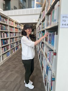 Woman in the library looking at books on the shelf about to pull one from the shelf