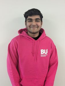 Male student looking to camera smiling wearing pink hooded jumper