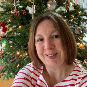 Tina is smiling at the camera, wearing a red and white striped top with a Christmas tree behind her