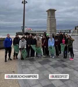 Group of students stood with litter bags on the beach, before a beach clean
