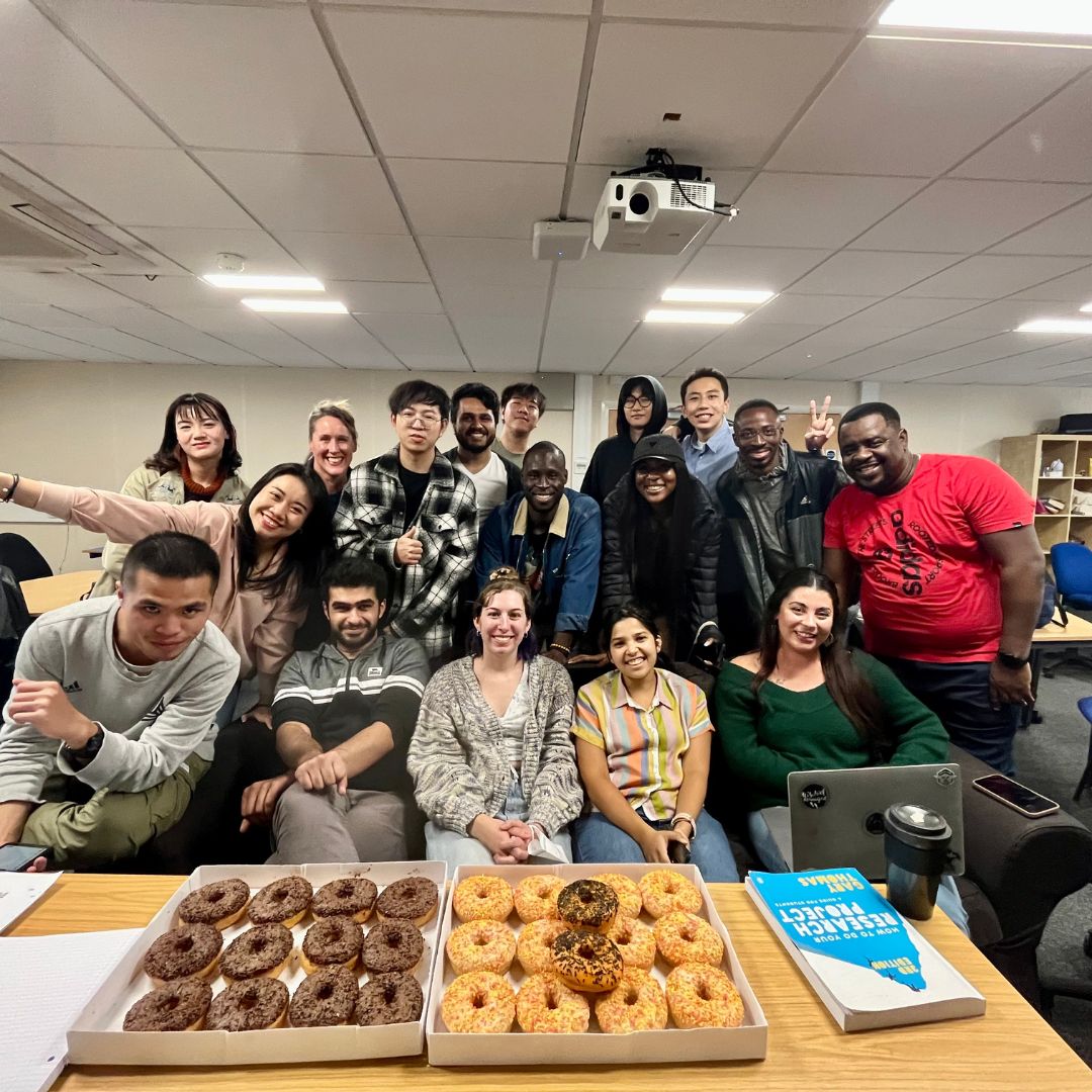 17 MA Producing for Film & Television students smile in a group photo with trays of doughnuts after getting to know one another in their first few weeks on the degree.