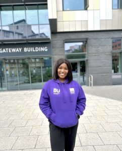 Keyia stands in front of a BU building wearing a purple BU hoodie
