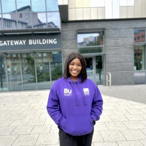 Keyia stands in front of a BU building wearing a purple BU hoodie