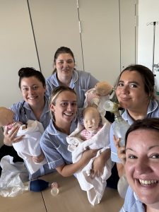 Zoe with her friends holding baby manikins and smiling at the camera