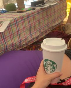 A person's hand holding a takeaway reusable Starbucks cup in the Herbal tea at the Faith and Reflection tent (Freshers Fair)