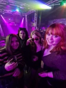 Photograph of 4 women dancing at DYMK club, holding drinks, pink lights