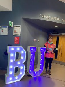 Sarah stands outside the create lecture theatre next to the big BU light up signs