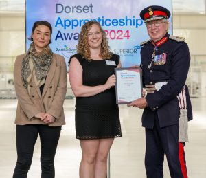 Three people standing up looking to camera. The woman in the middle is recieving an award at the Dorset Apprenticeship Awards