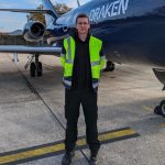 Young man standing in front of a plane wearing a high vis jacket