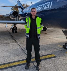 Elliot standing in front of a plane wearing a high vis jacket