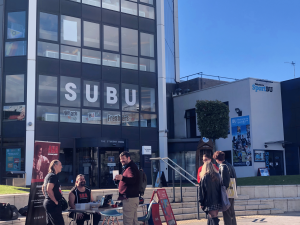 A crowd of people outside the SUBU building on a sunny day