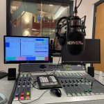 Photo of the Nerve Radio studio which shows two computer screens, a microphone and a mixing desk.