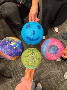 Students displaying four colourful, hand-decorated balls in a campus craft activity.