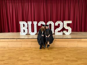 Osher and her friend with gowns at their graduation with BU 2025 sign behind them.